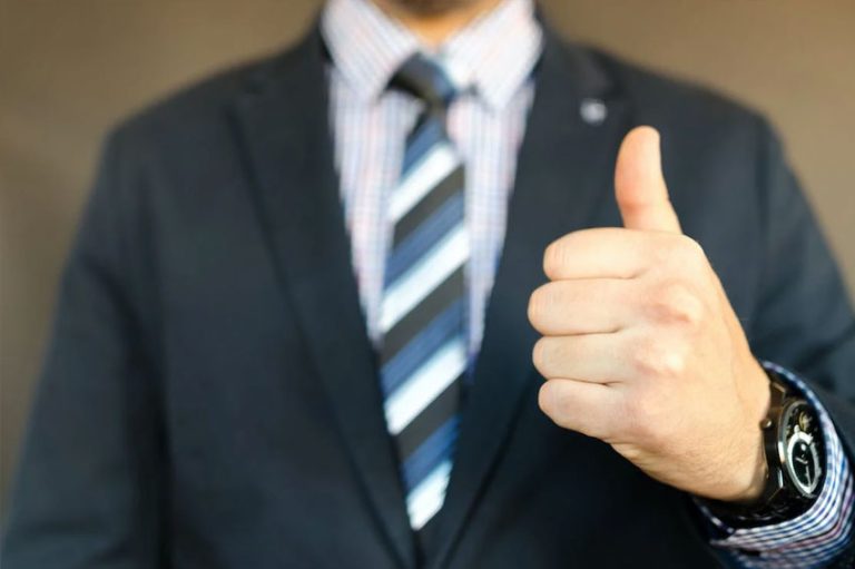 Homem de terno fazendo sinal de legal com a mão.